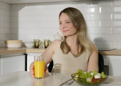 Smiling woman enjoying a healthy meal with salad and orange juice in a modern kitchen.