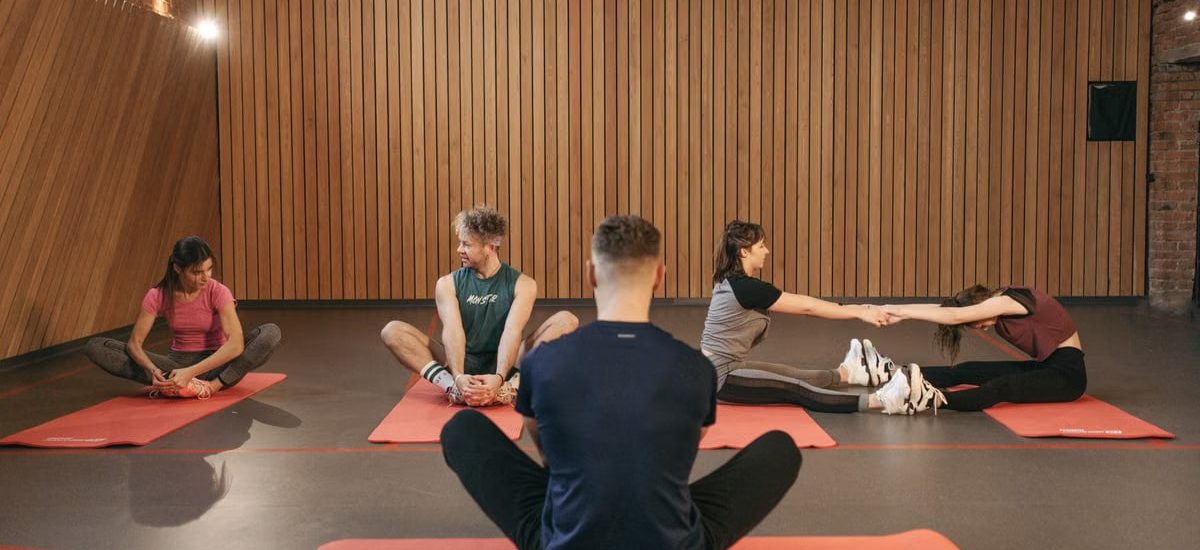 A group of adults practicing yoga and stretching on mats in a wooden panelled room.