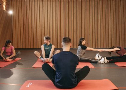 A group of adults practicing yoga and stretching on mats in a wooden panelled room.